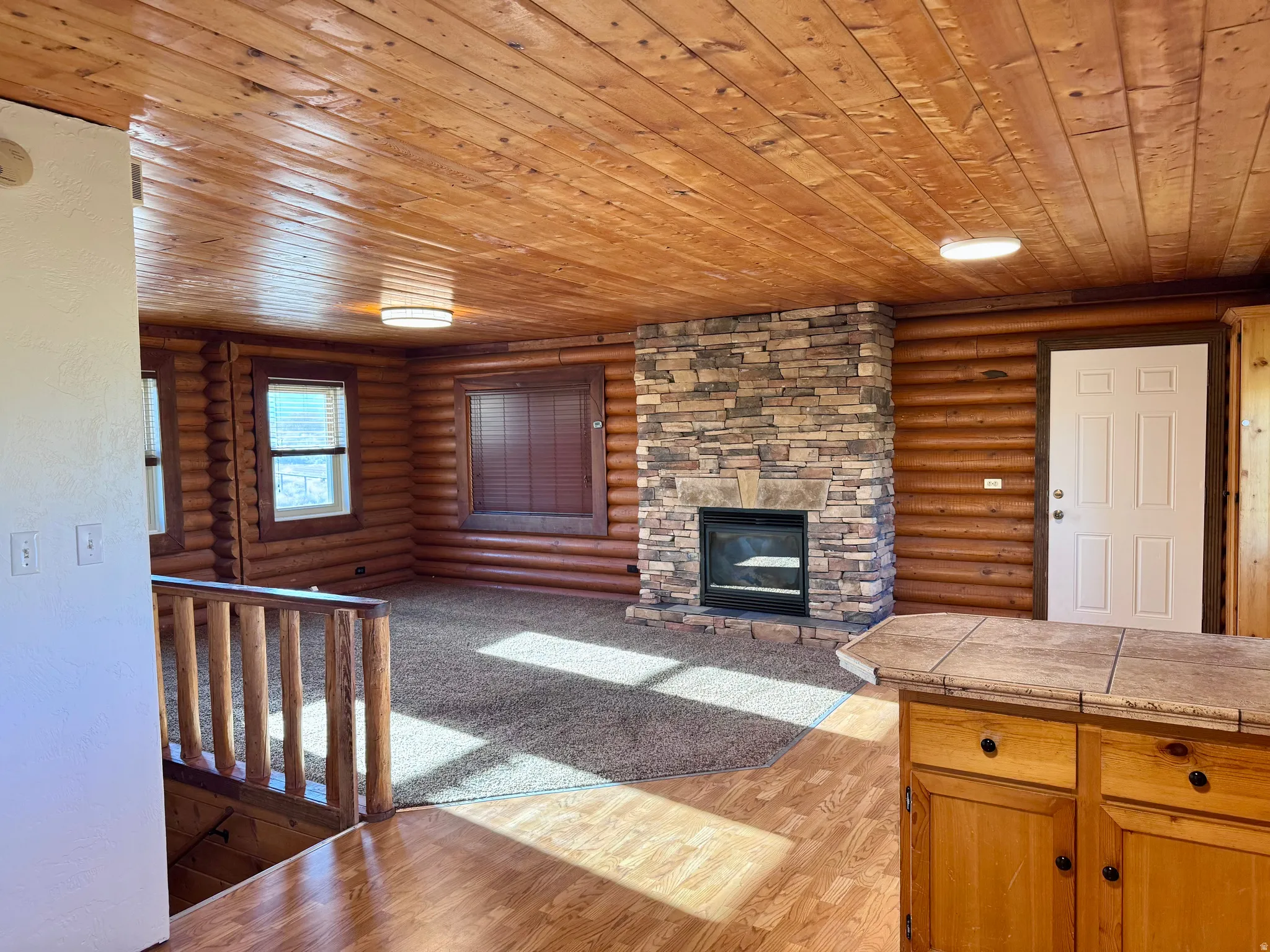 Log-style interior featuring a stone-clad fireplace, wood-finish plank ceiling, and wood-finish flooring