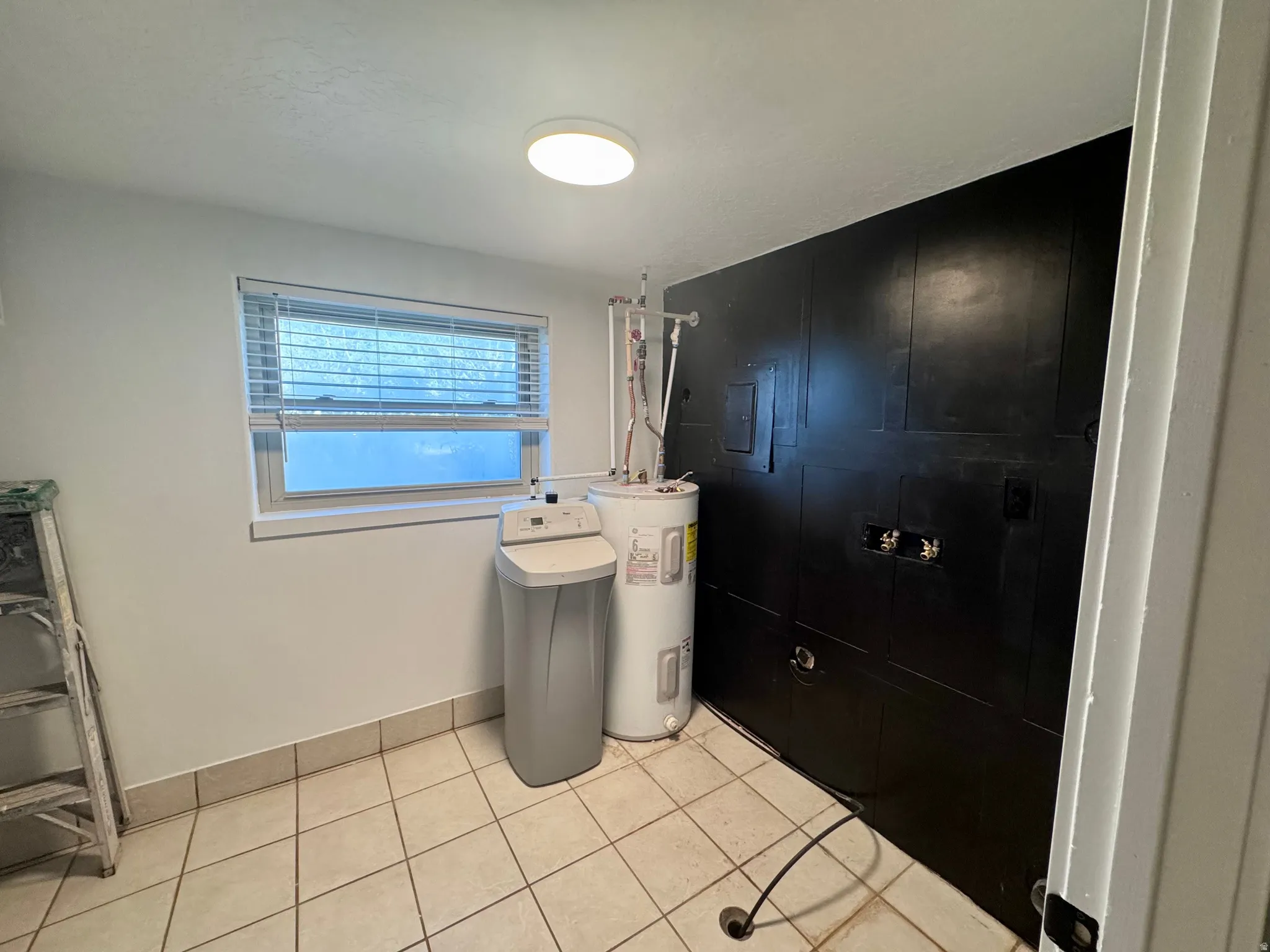Interior utility room featuring tiled flooring, a window with blinds, and a ceiling-mounted light fixture