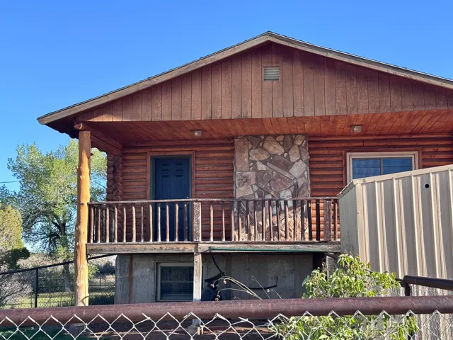 Log cabin exterior featuring a second-story balcony with wood railing, natural stone facade detailing, and wood-finish siding