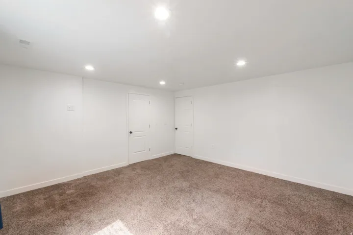 Spacious room featuring neutral carpeting, white walls, recessed ceiling lighting, and two panel doors with dark hardware
