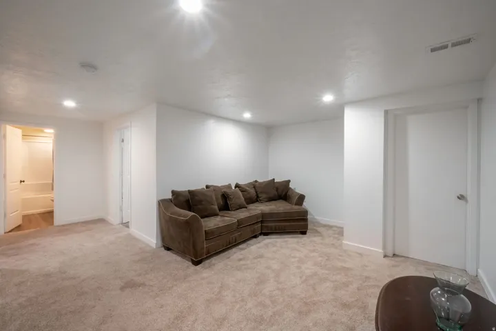 Spacious room with recessed lighting, light-toned carpet flooring, white walls, and white trim, featuring a partial view of a bathroom with a white tub/shower combination and wood-finish flooring