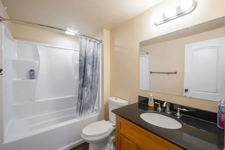 Bathroom featuring a white tub-shower combination unit, a toilet, and a vanity with a dark countertop and an undermount sink