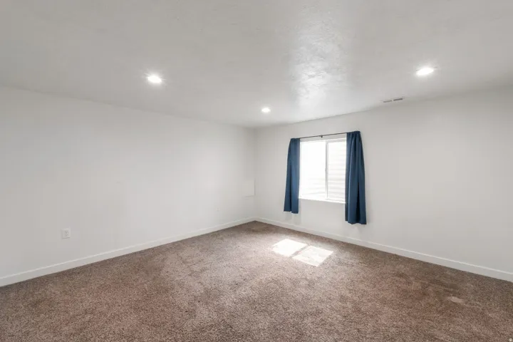 Spacious room featuring neutral carpeting, white baseboards, and recessed ceiling lighting