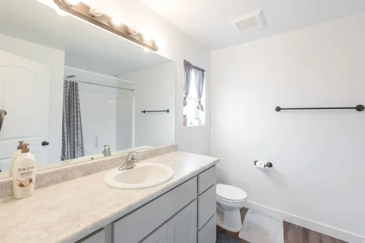 Bathroom featuring a light-toned vanity with an integrated sink, a large wall-mounted mirror, and a multi-bulb light fixture