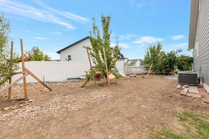 Expansive backyard area featuring a white privacy fence, young trees, and a concrete pad