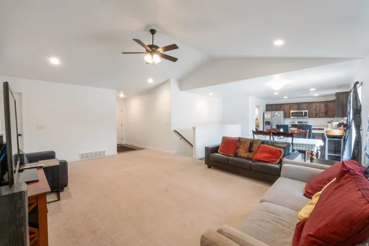 Open-concept living area featuring light-toned carpeting, recessed ceiling lighting, and a ceiling fan