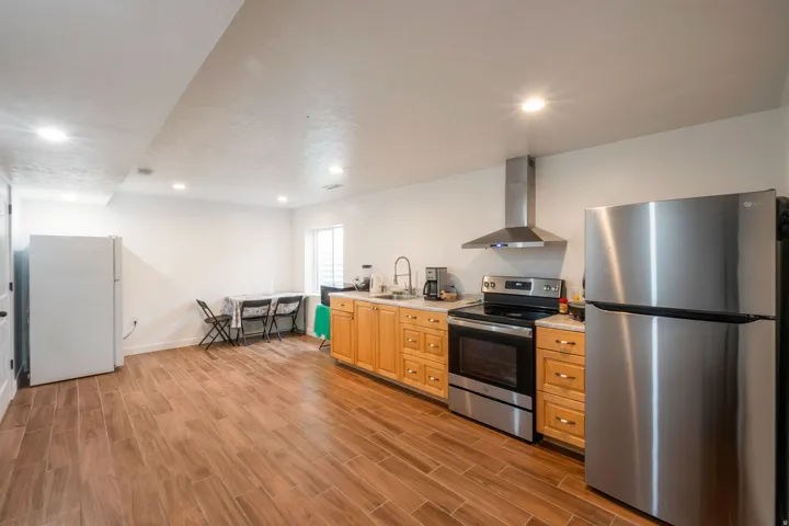 Kitchen area featuring wood-finish flooring, light wood cabinetry, stainless steel appliances, a stainless steel range hood, and recessed lighting