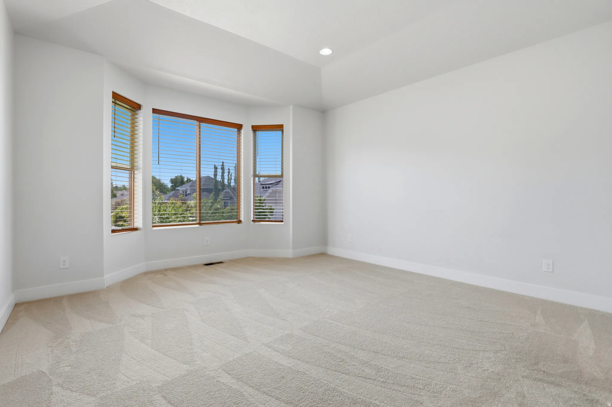Spacious room featuring a bay window with natural wood trim and horizontal blinds, recessed ceiling lighting, and light-toned carpeting