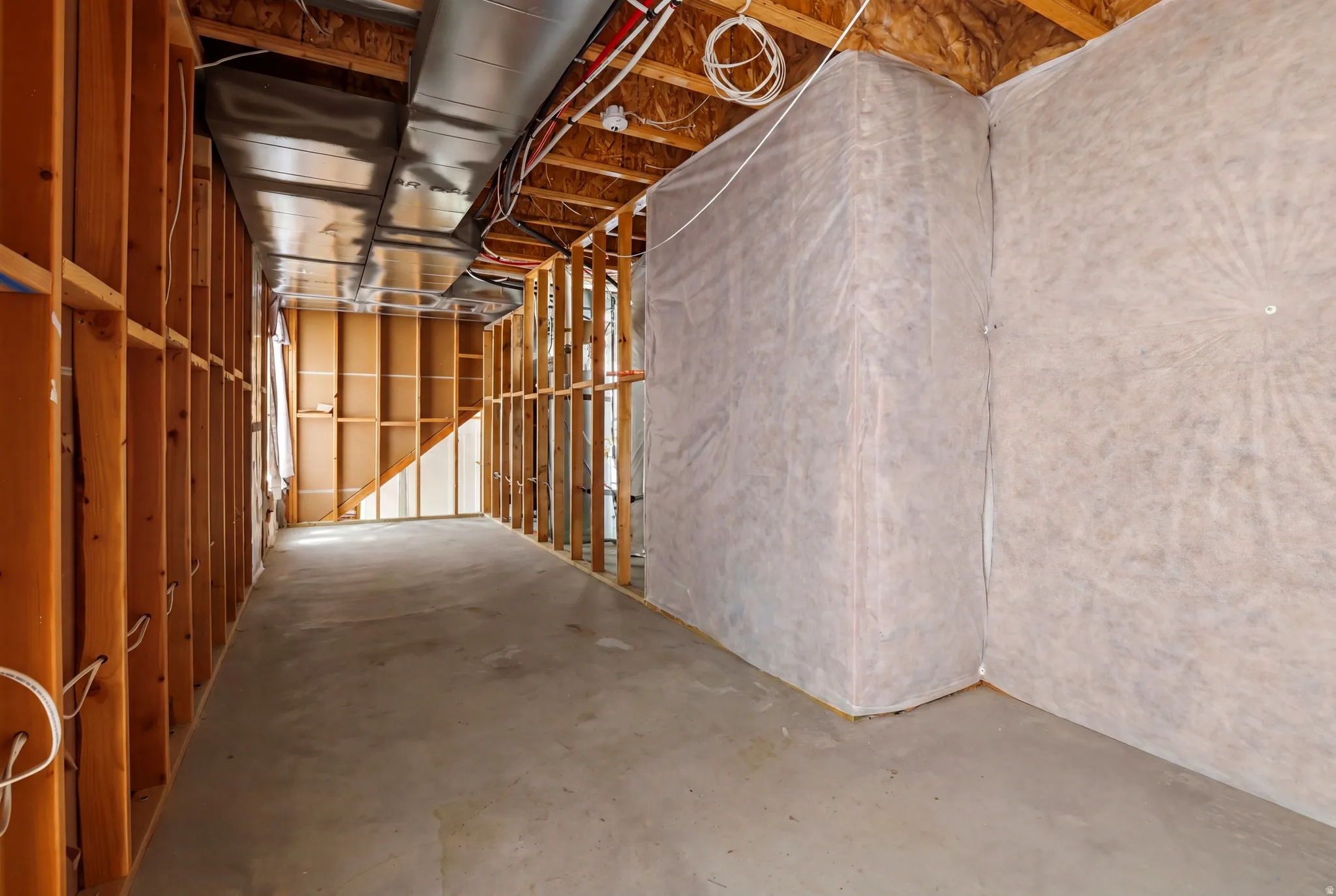 Unfinished basement framing with exposed lumber studs, concrete flooring, insulated perimeter walls, visible ductwork, and electrical conduit