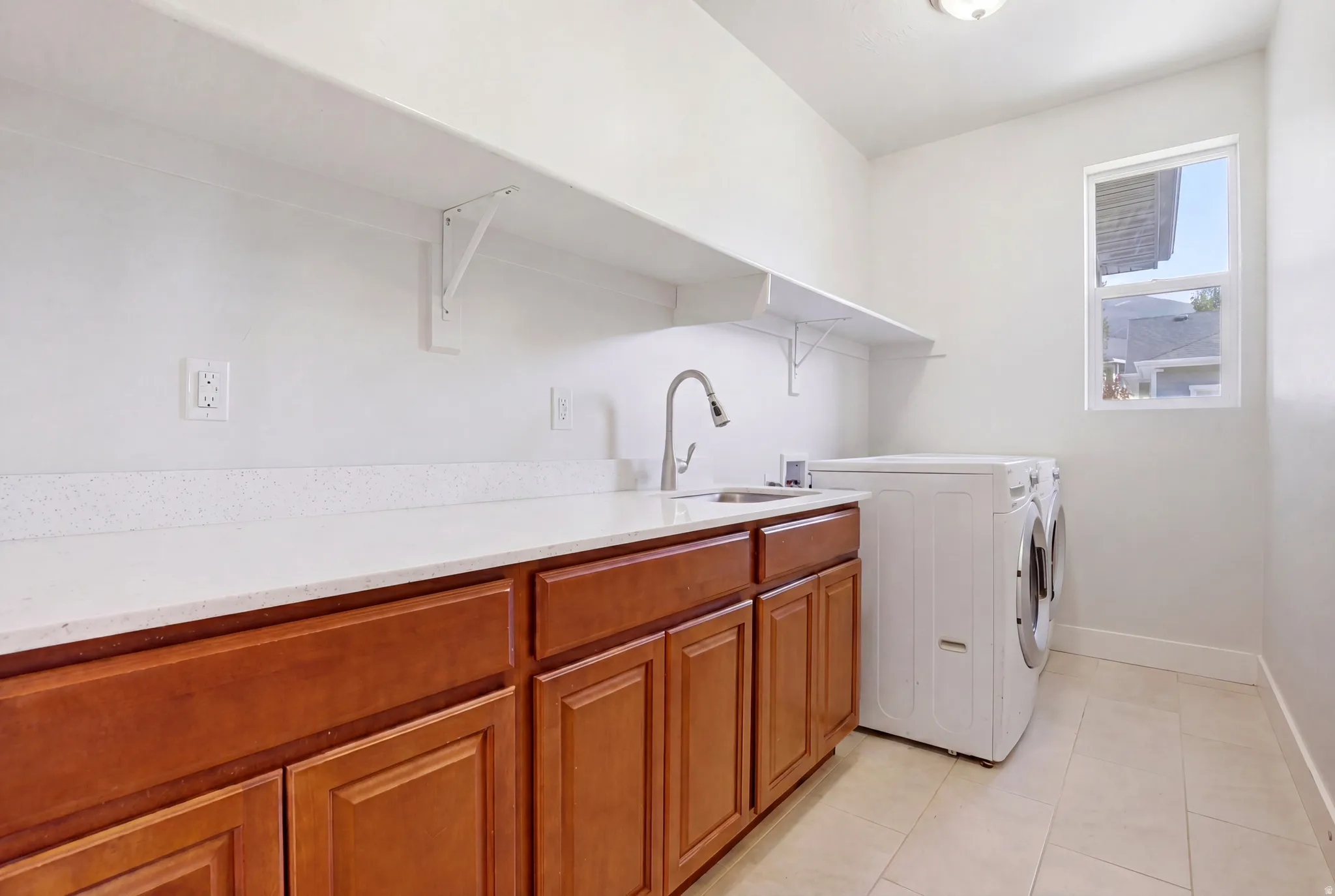 Laundry room featuring wood-finish cabinetry, light-toned countertops, and a stainless steel sink with a gooseneck faucet