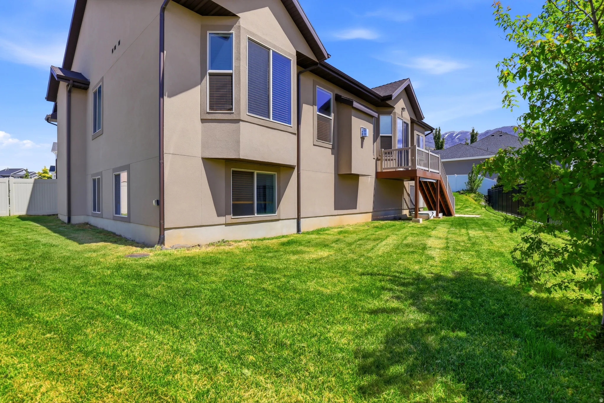 Expansive rear yard featuring a manicured lawn, multi-level deck with railing, and stucco exterior with multiple windows
