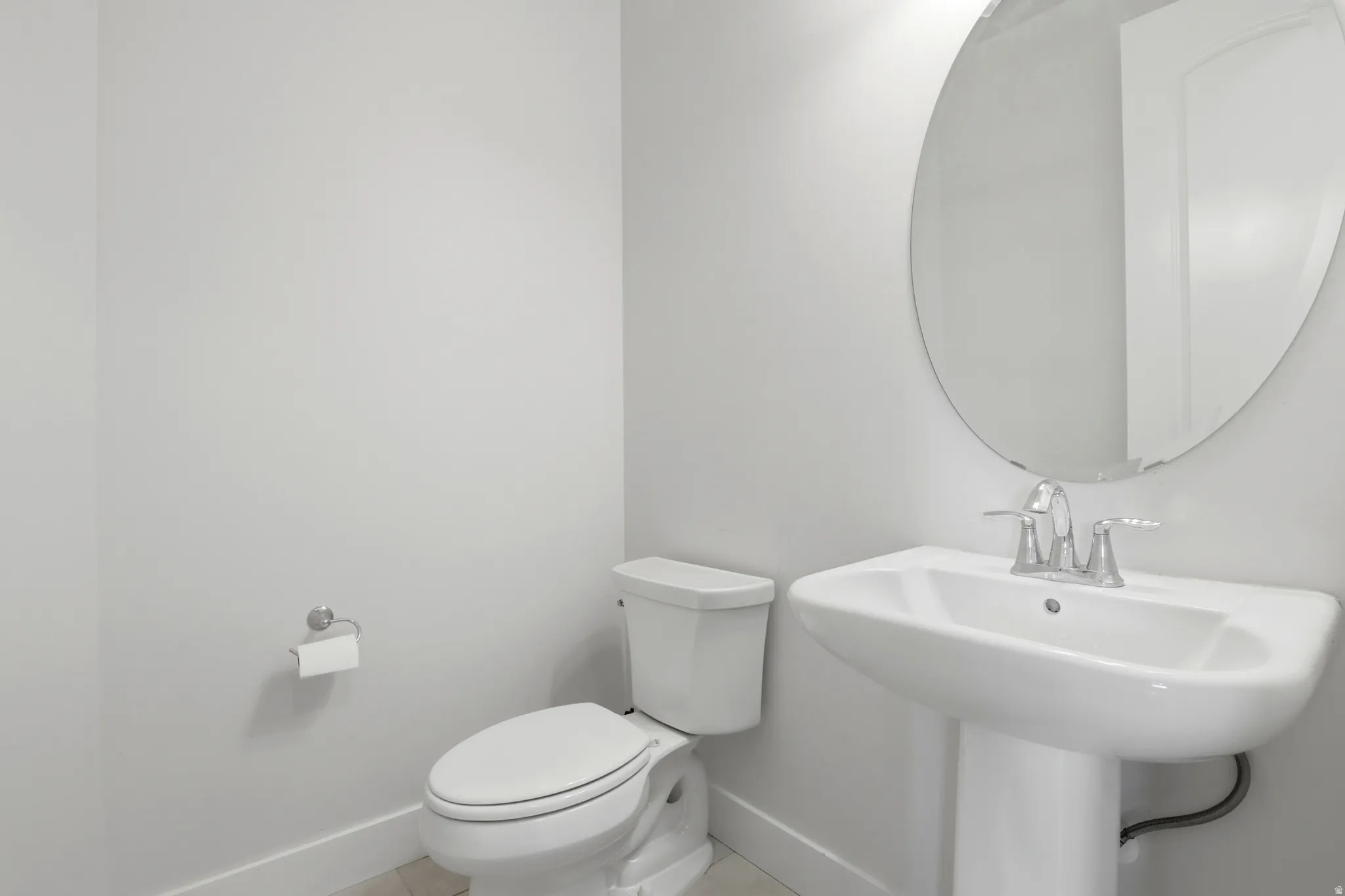 Pedestal sink with chrome faucet, oval mirror, and white toilet