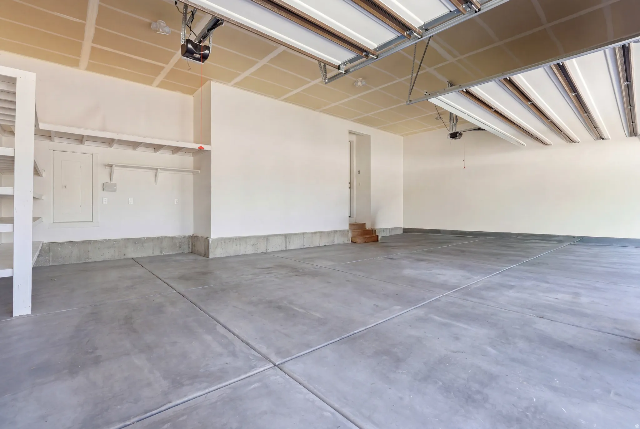 Spacious garage featuring a concrete floor, built-in shelving, overhead lighting, and an automatic garage door opener