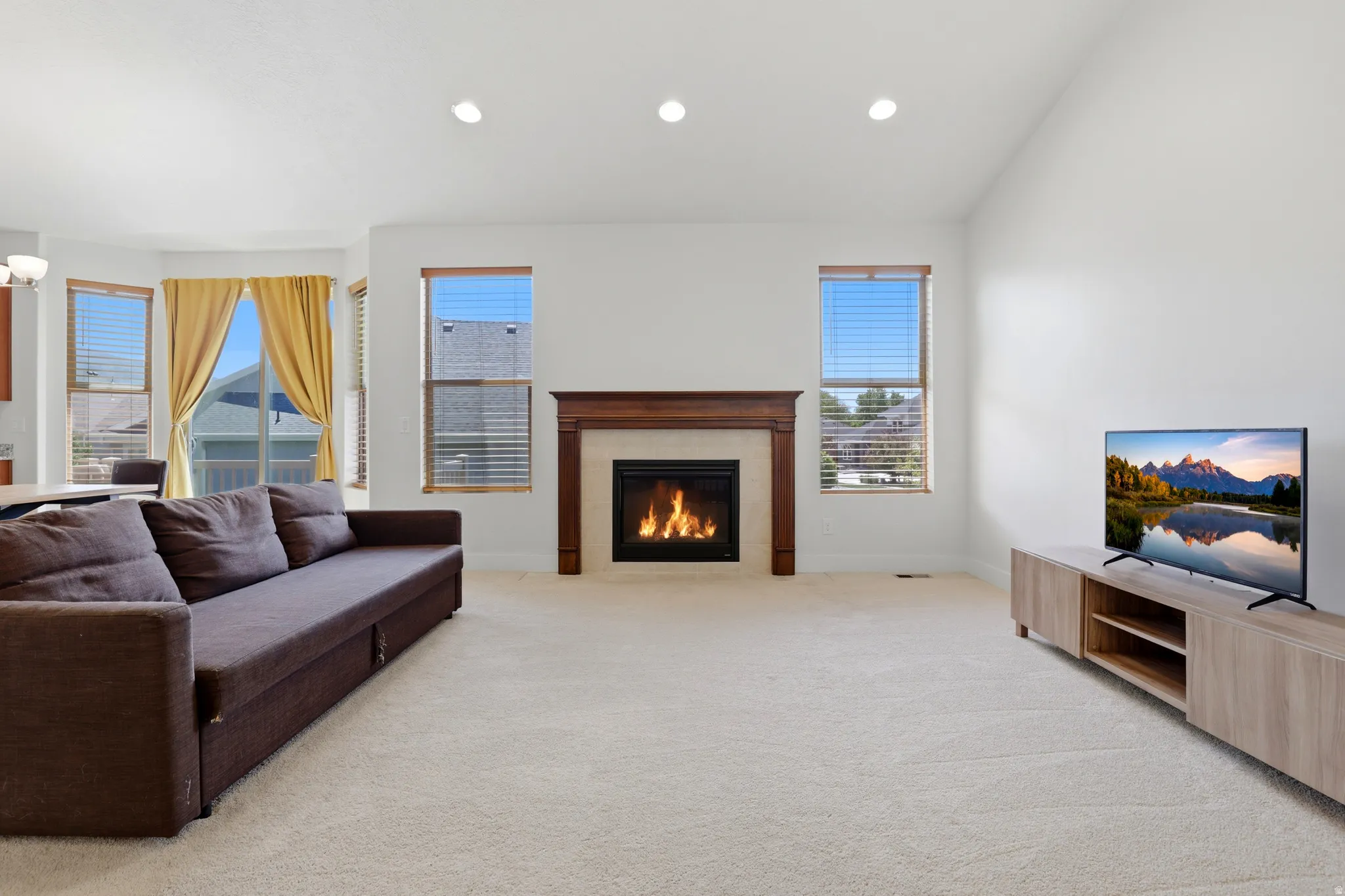 Living area featuring a fireplace with a wood mantle and stone surround, recessed lighting, and light-colored carpet flooring