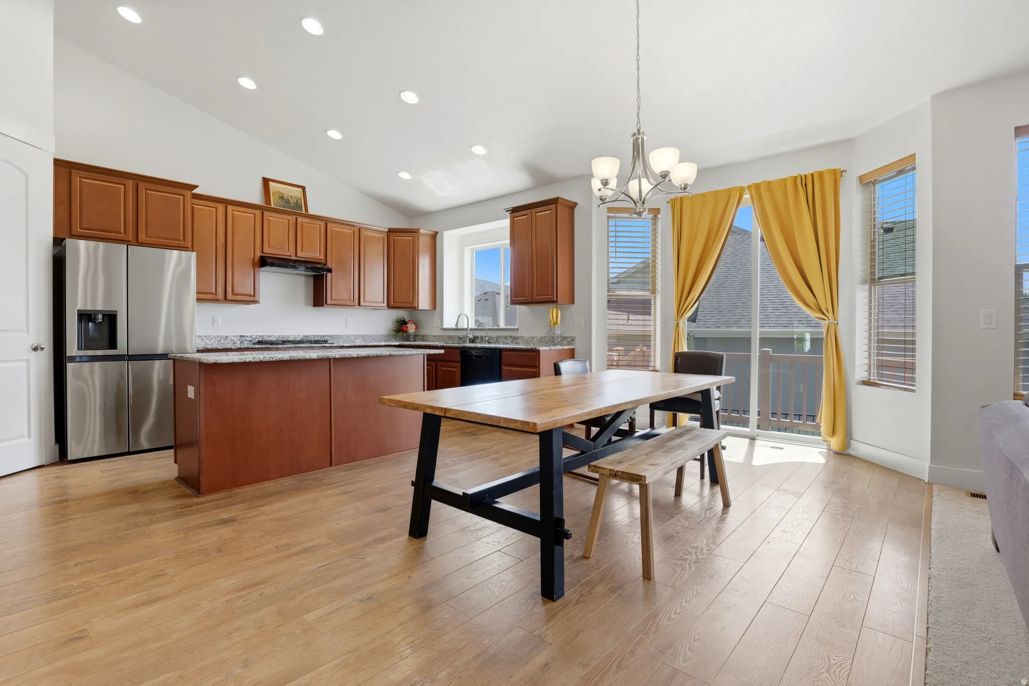 Open-concept kitchen and dining area featuring wood-finish flooring, vaulted ceilings, and recessed lighting