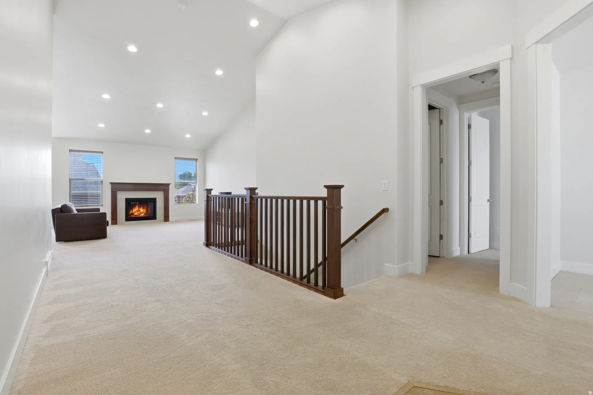 Carpeted landing with dark wood railing overlooking a vaulted living area