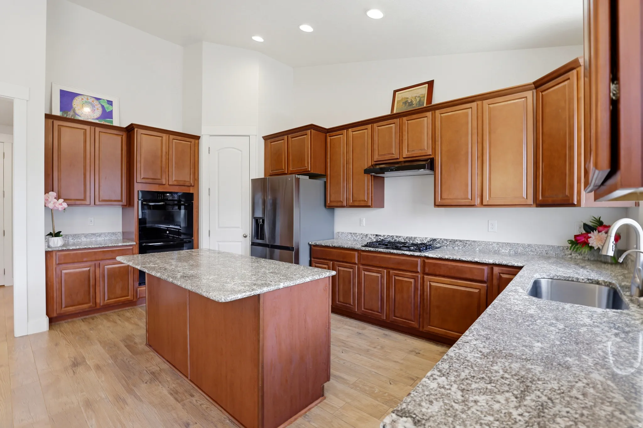 Well-appointed kitchen featuring light wood-finish flooring, a central island with granite countertop, abundant wood cabinetry, stainless steel appliances, and recessed lighting