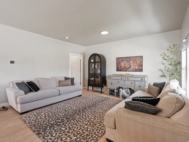Spacious living area featuring light-toned walls, wood-finish flooring, recessed lighting, and a large window with striped valance