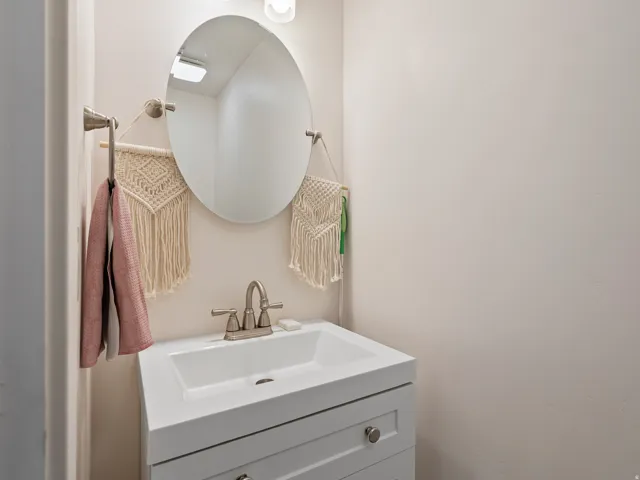 Vanity area featuring a white rectangular sink, brushed nickel faucet, and a wall-mounted oval mirror