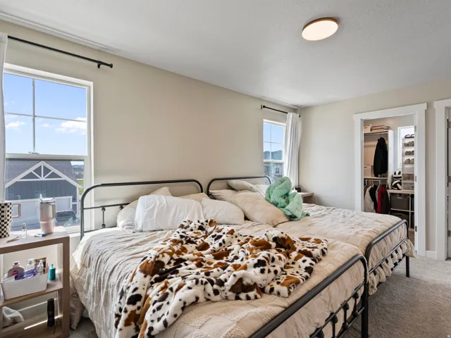 Carpeted bedroom featuring two large windows, a built-in closet with shelving, and a ceiling-mounted light fixture