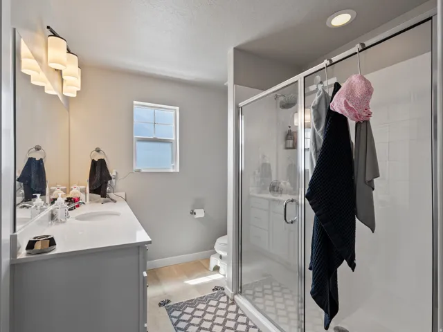 Bathroom featuring a glass-enclosed shower, a double vanity with a light-toned countertop, and light wood-finish flooring