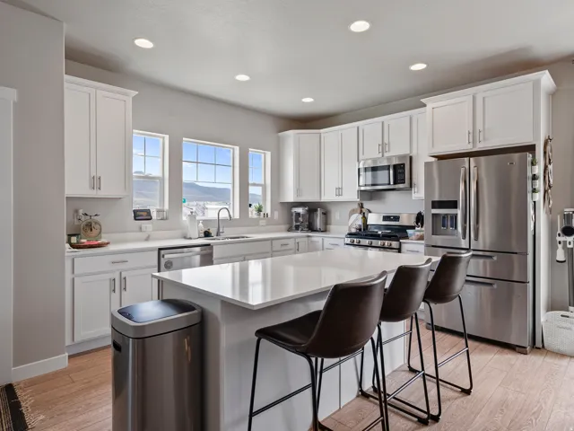 Modern kitchen featuring white shaker cabinetry, stainless steel appliances, a large center island with a solid surface countertop, wood-finish flooring, and ample recessed lighting