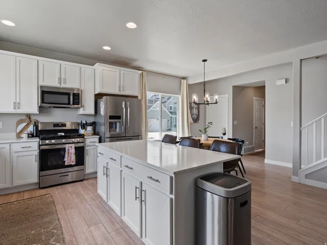 Open-concept kitchen featuring an expansive central island with a solid surface countertop, white shaker cabinetry with brushed nickel hardware, and stainless steel appliances