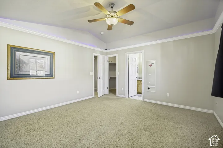 Spacious room featuring vaulted ceilings with a ceiling fan, crown molding, and neutral-toned carpet flooring
