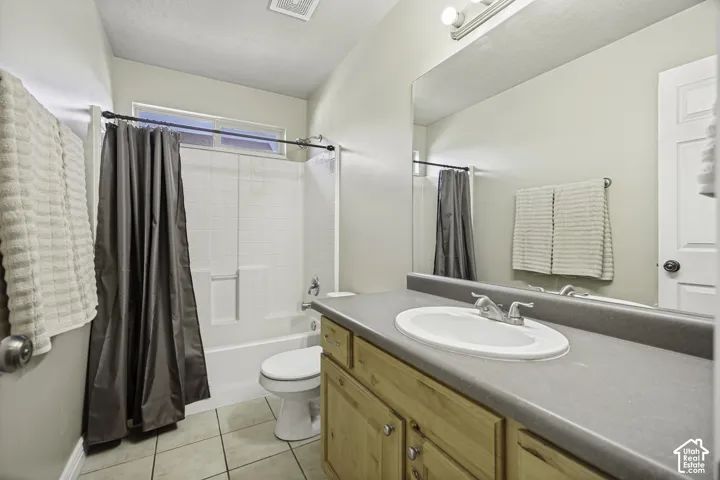 Bathroom featuring a single vanity with wood-finish cabinetry, a large integrated mirror, a shower-tub combination, a toilet, and light-toned tile flooring