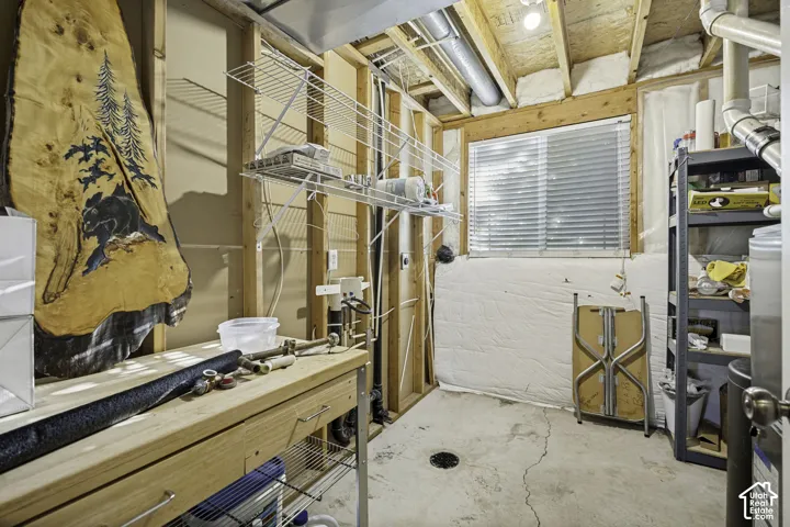 Unfinished basement space featuring exposed wood framing, a built-in workbench, and a window providing natural light