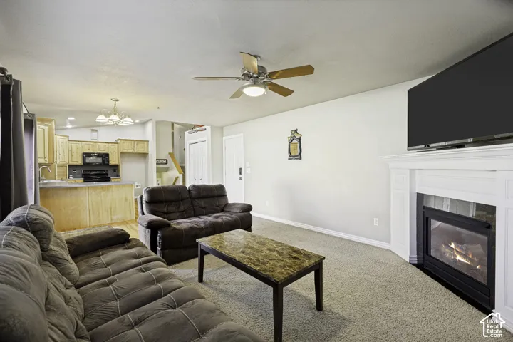 Living area featuring a white mantel fireplace, ceiling fan with integrated lighting, and carpet flooring