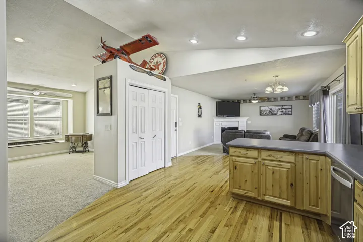 Open-concept living area featuring wood-finish flooring, a kitchen island with light wood cabinetry, recessed lighting, and a fireplace with a white mantel