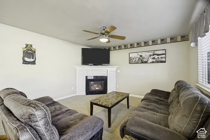 Living area featuring a corner fireplace with a white mantel, ceiling fan with integrated lighting, and carpeted flooring
