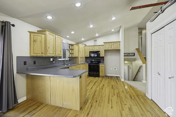 Kitchen featuring natural wood cabinetry, dark countertops, a built-in black range and microwave, and wood-finish flooring