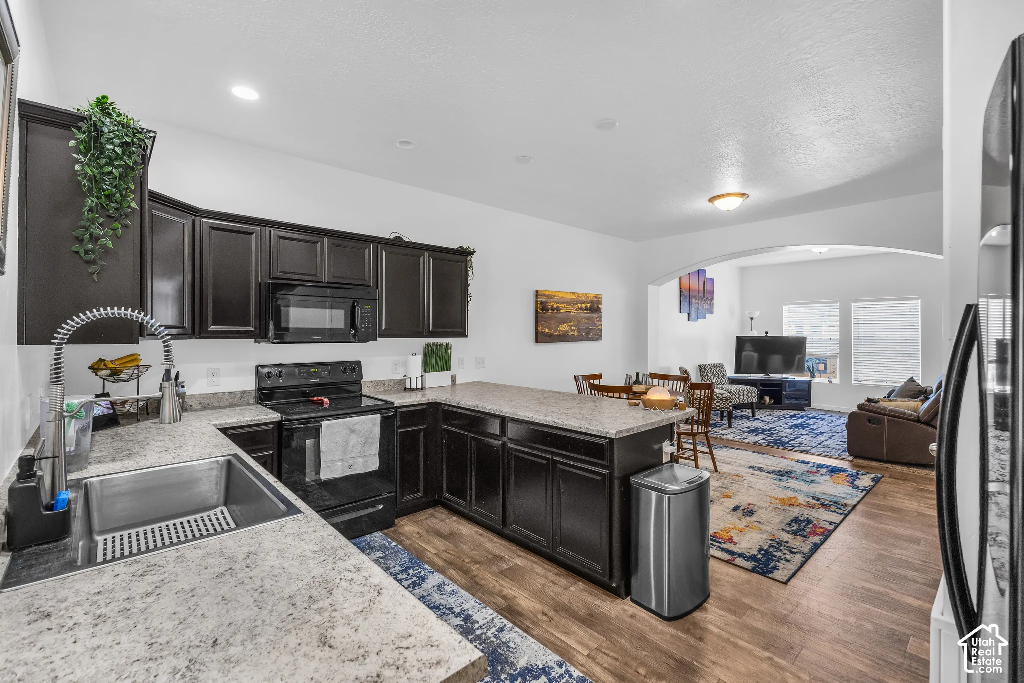 Open-concept kitchen featuring dark cabinetry, light-toned countertops, and wood-finish flooring