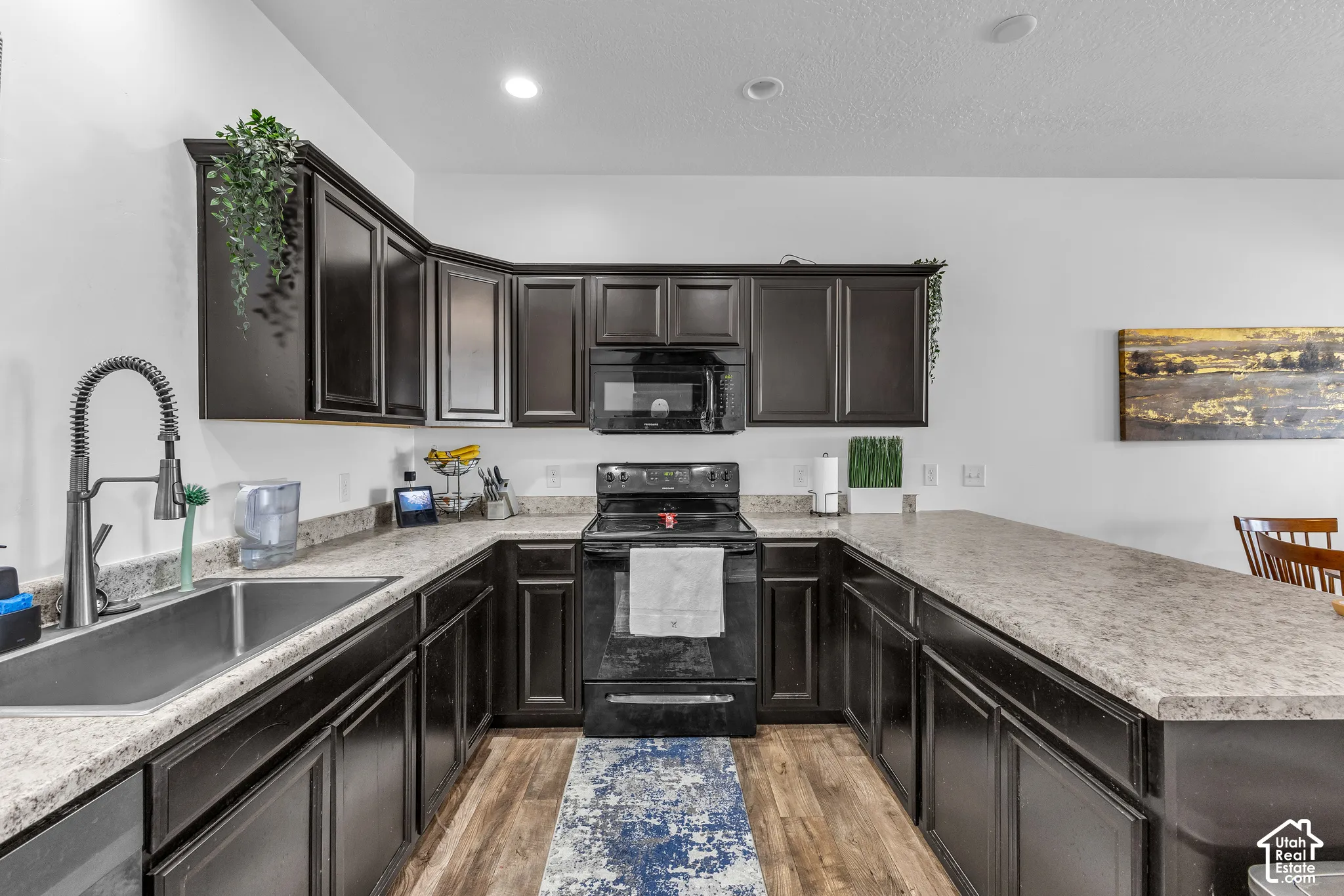 U-shaped kitchen featuring dark wood-finish cabinetry, light-toned countertops, and a stainless steel double basin sink with a high-arc faucet