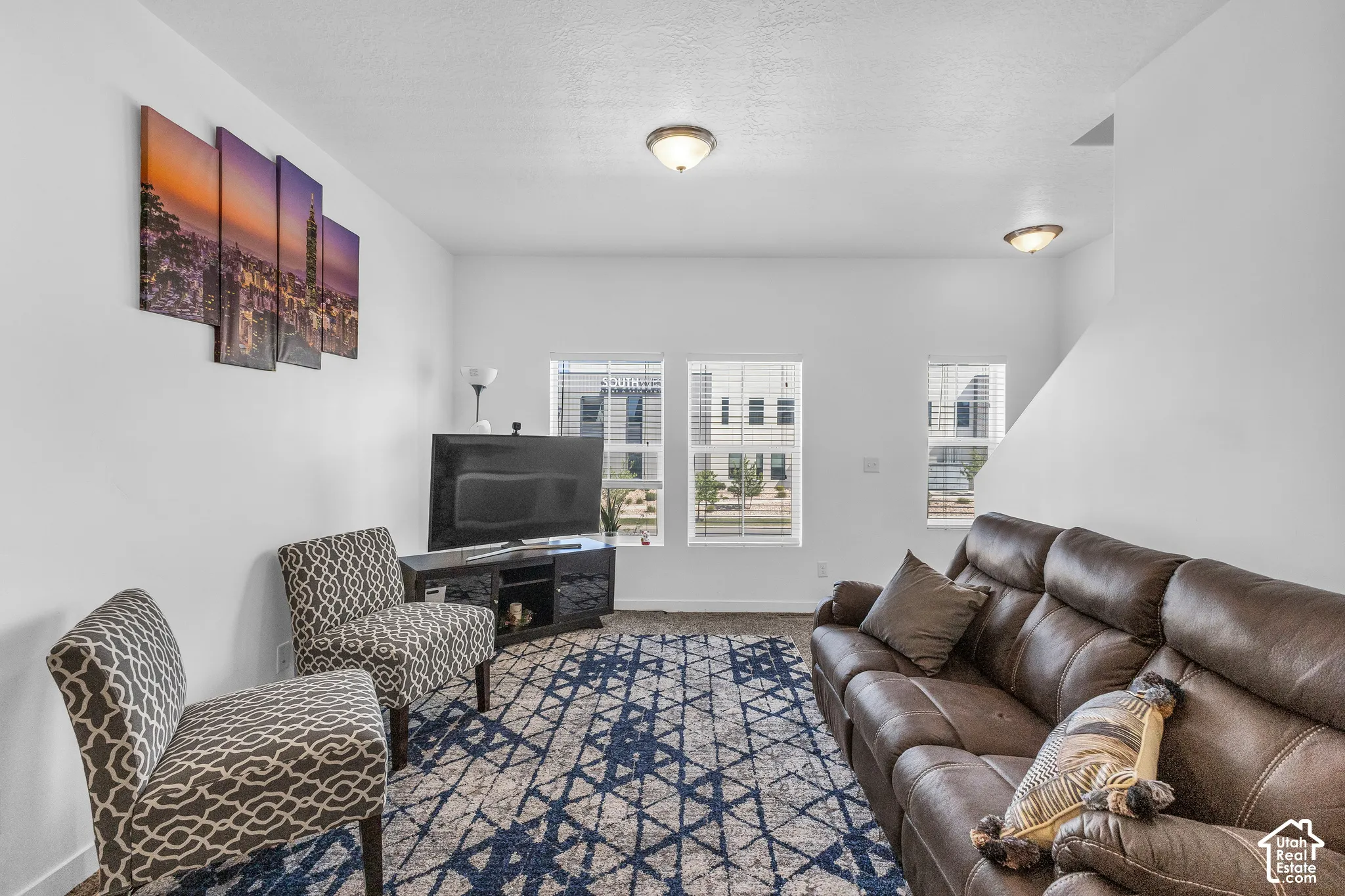 Bright living area featuring white walls, two windows with blinds, and ceiling-mounted light fixtures
