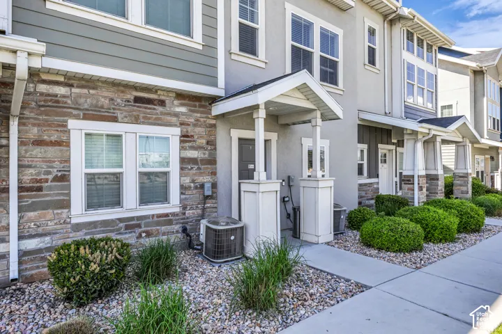 Townhome exterior featuring stacked stone accents, horizontal siding, multiple windows, a covered entry, and concrete pathways with decorative gravel and plantings