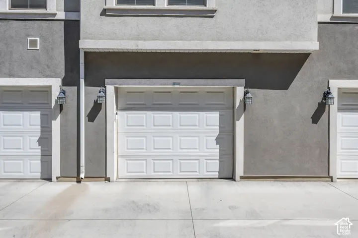 Stucco exterior featuring multiple white paneled garage doors, decorative outdoor lighting fixtures, and a concrete driveway