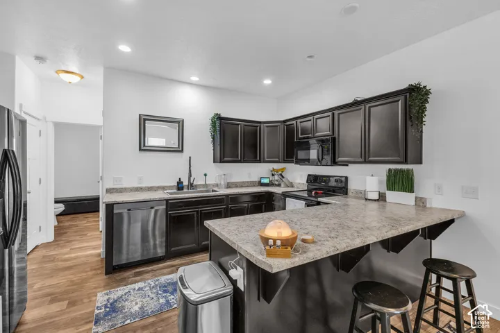 Modern kitchen featuring dark cabinetry, light-colored countertops, stainless steel appliances, wood-finish flooring, and recessed lighting