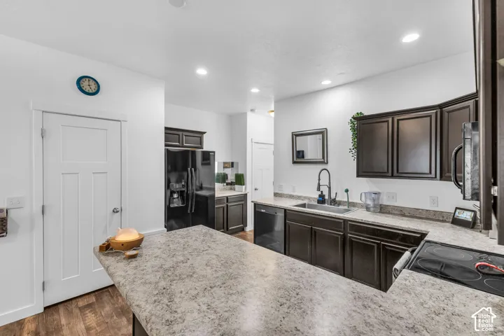 Kitchen featuring dark wood cabinetry, light-colored countertops, a built-in stainless steel sink with a gooseneck faucet, a built-in cooktop, and wood-finish flooring