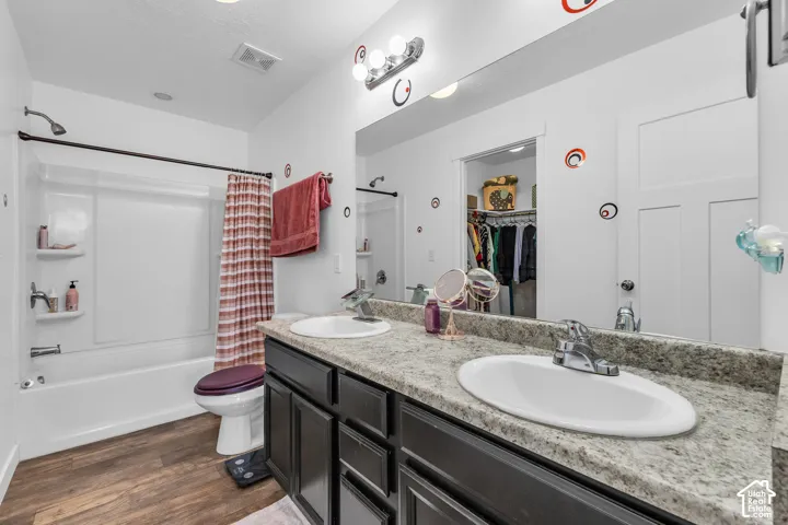 Bathroom featuring a dual-sink vanity with a light granite-finish countertop, dark cabinetry, and wood-finish flooring