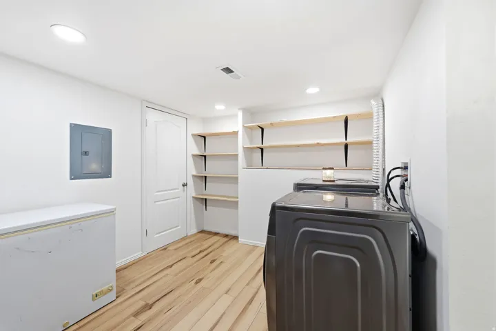 Laundry room with electric panel, light wood-style floors, recessed lighting, and washing machine and clothes dryer