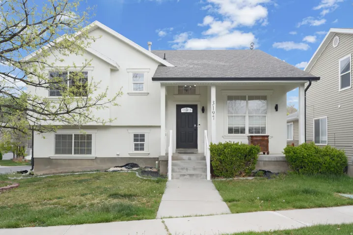Contemporary stucco exterior with a covered porch, dark entry door, multiple windows, and a landscaped front yard