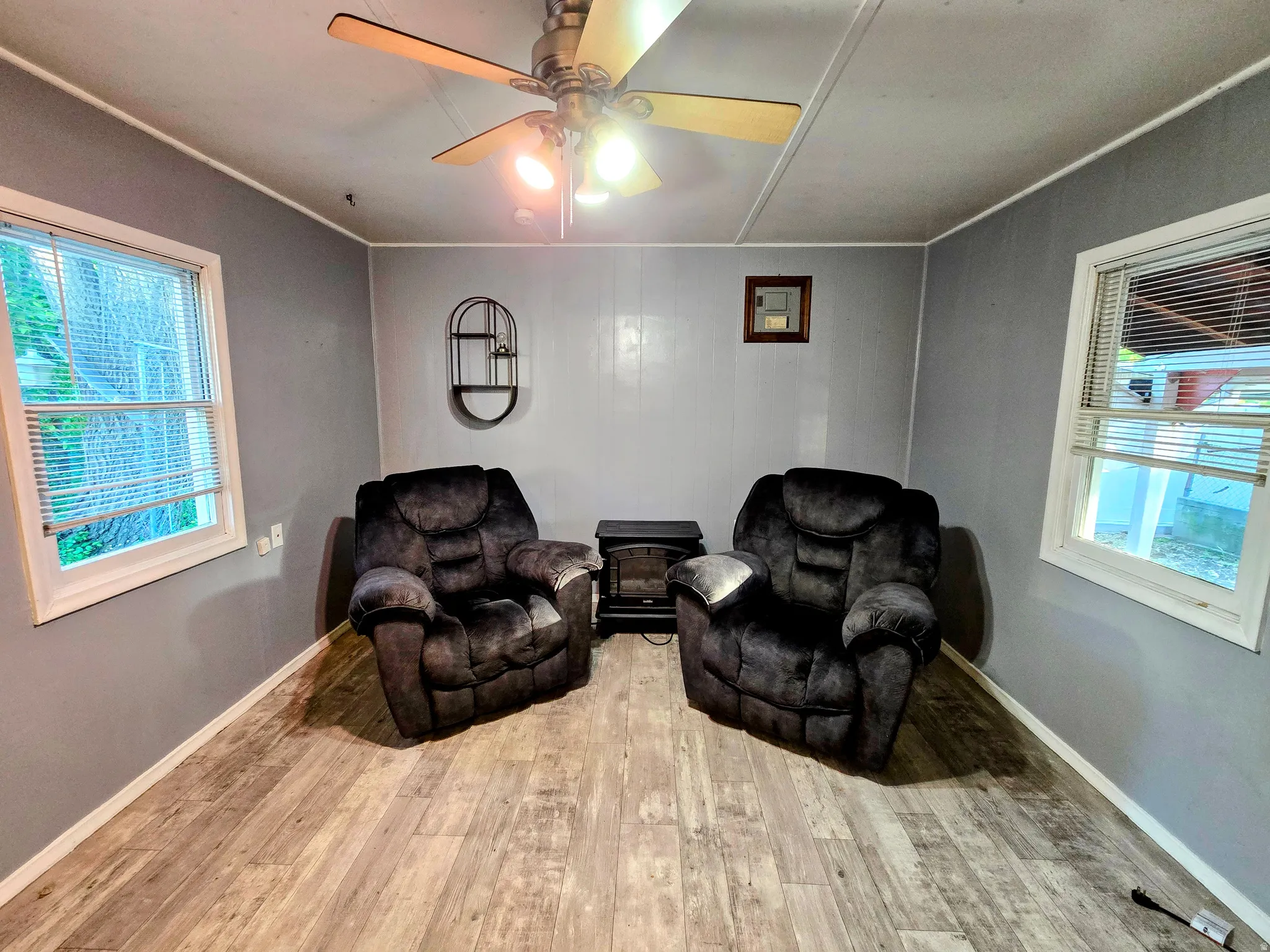 Room featuring wood-finish flooring, two windows with blinds, and a ceiling fan with integrated lighting