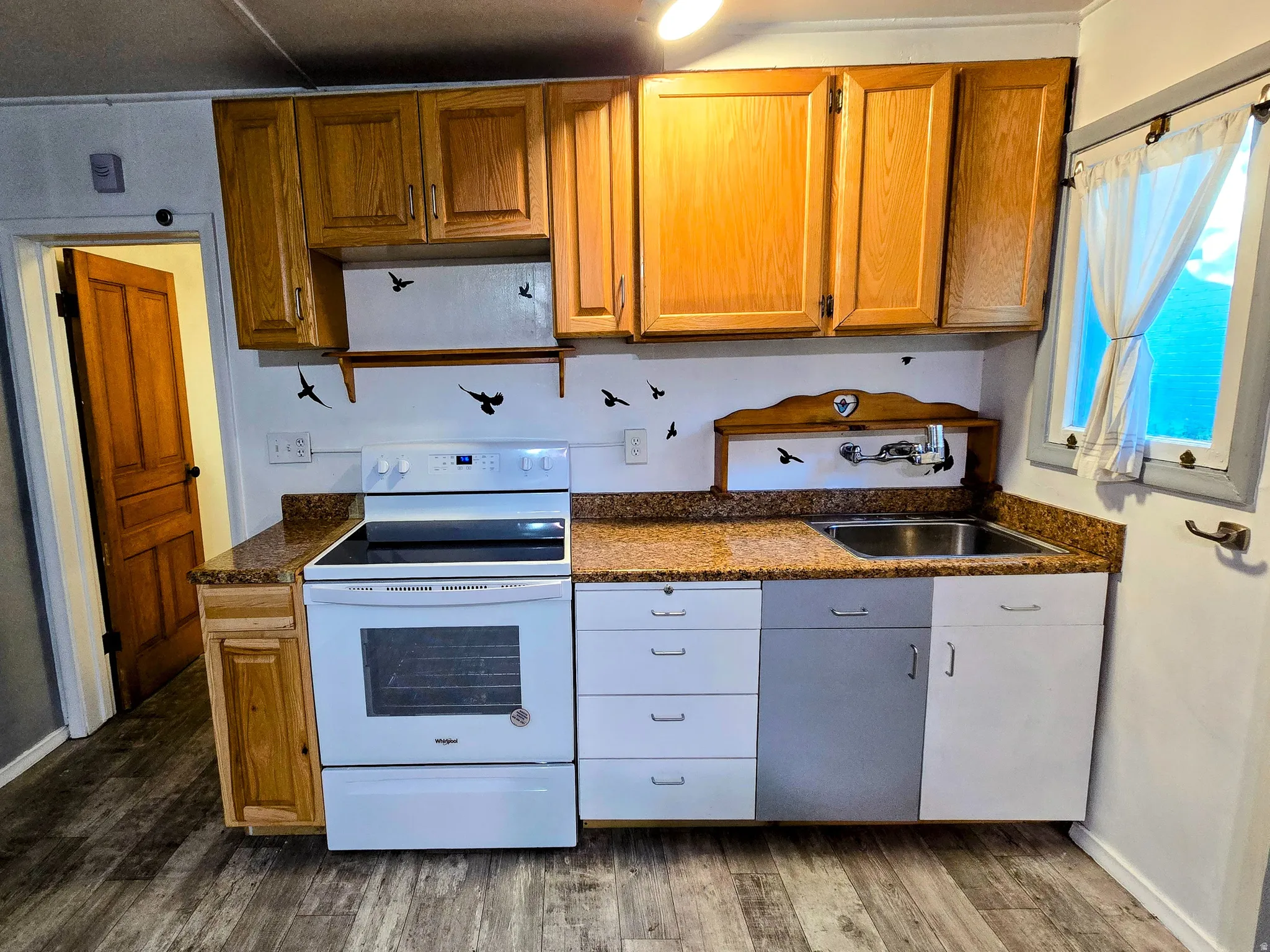 Kitchen featuring wood-finish flooring, wood cabinetry, stone-finish countertops, stainless steel sink, and white appliances