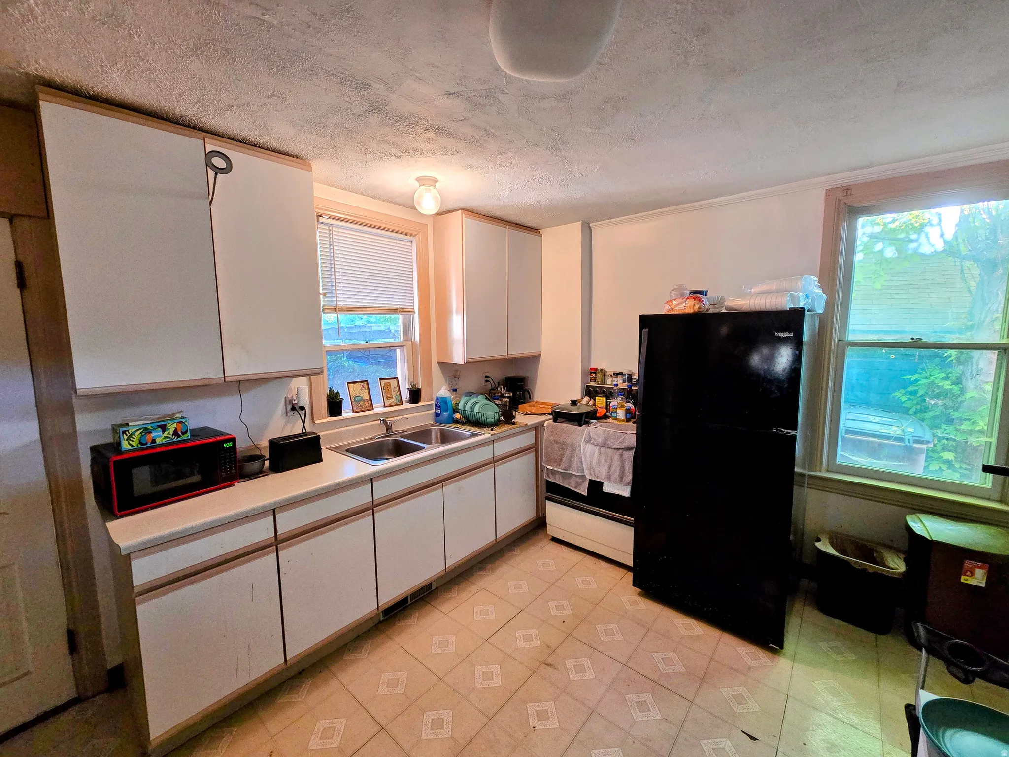 Kitchen featuring abundant cabinetry, dual windows, a double basin stainless steel sink, and patterned floor tiling