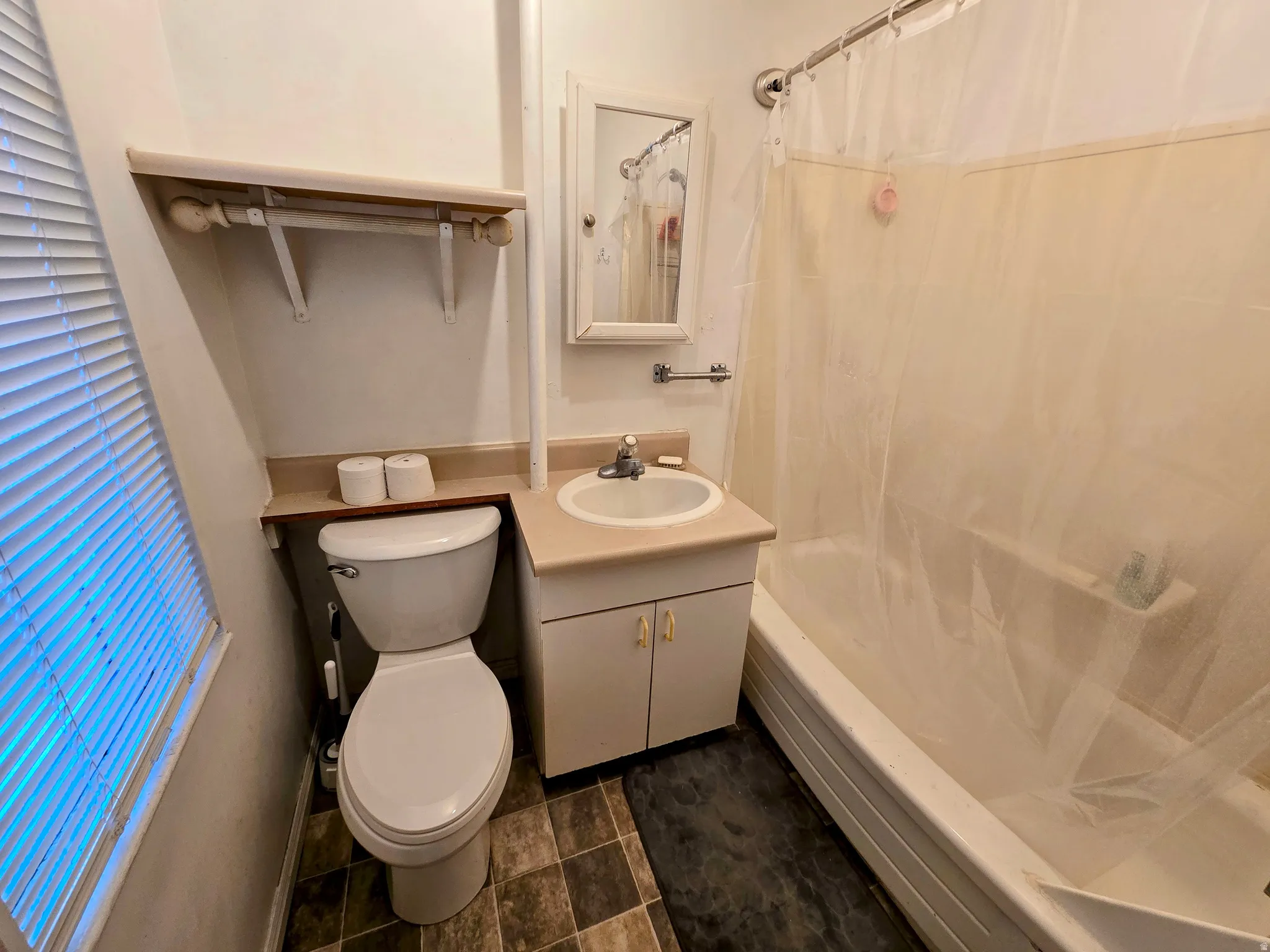 Bathroom featuring a white bathtub with shower, vanity with integrated sink, wall-mounted mirror, and a window with blinds