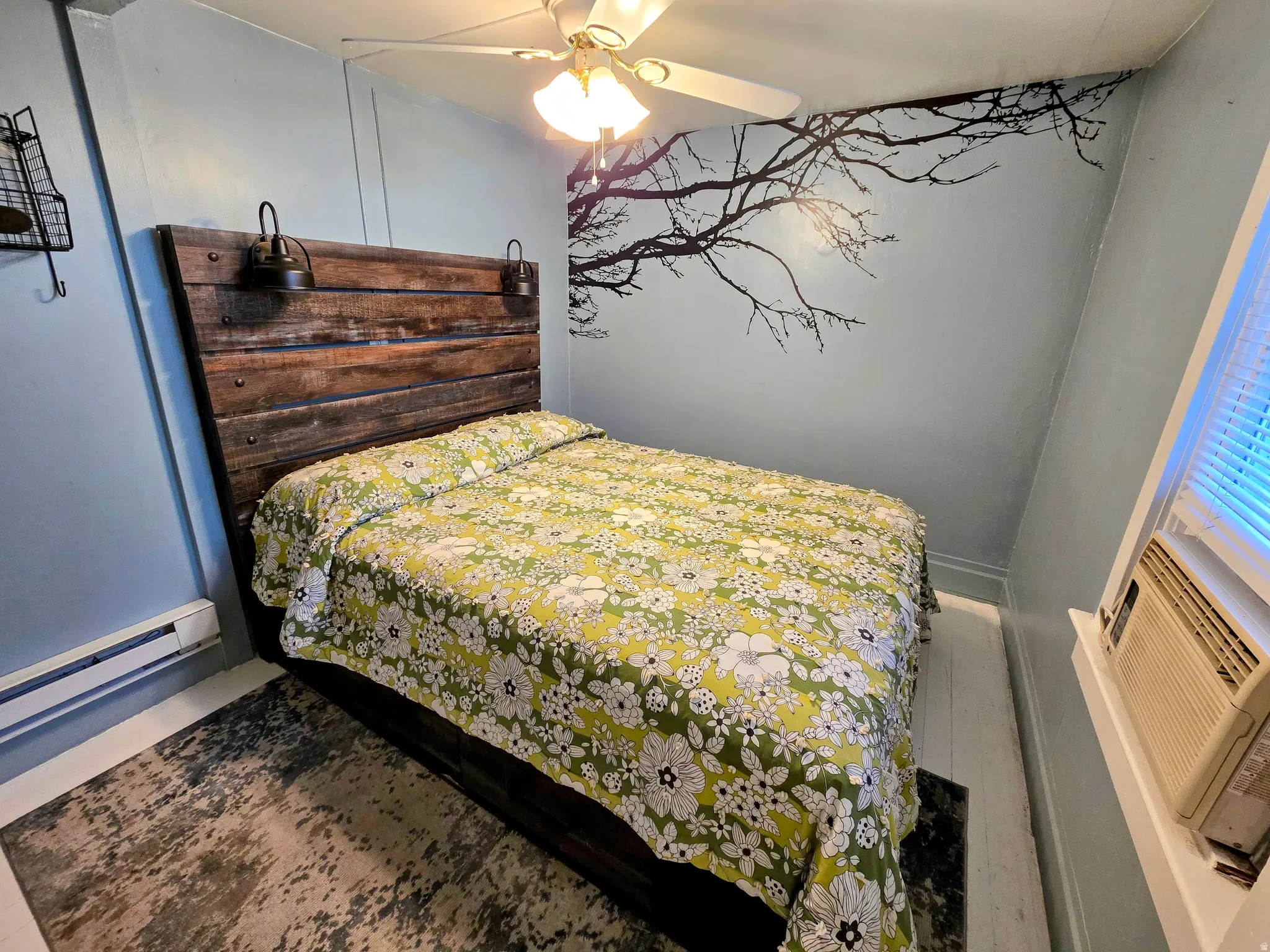Bedroom featuring a ceiling fan with light fixture, hardwood flooring, and a wall-mounted air conditioning unit