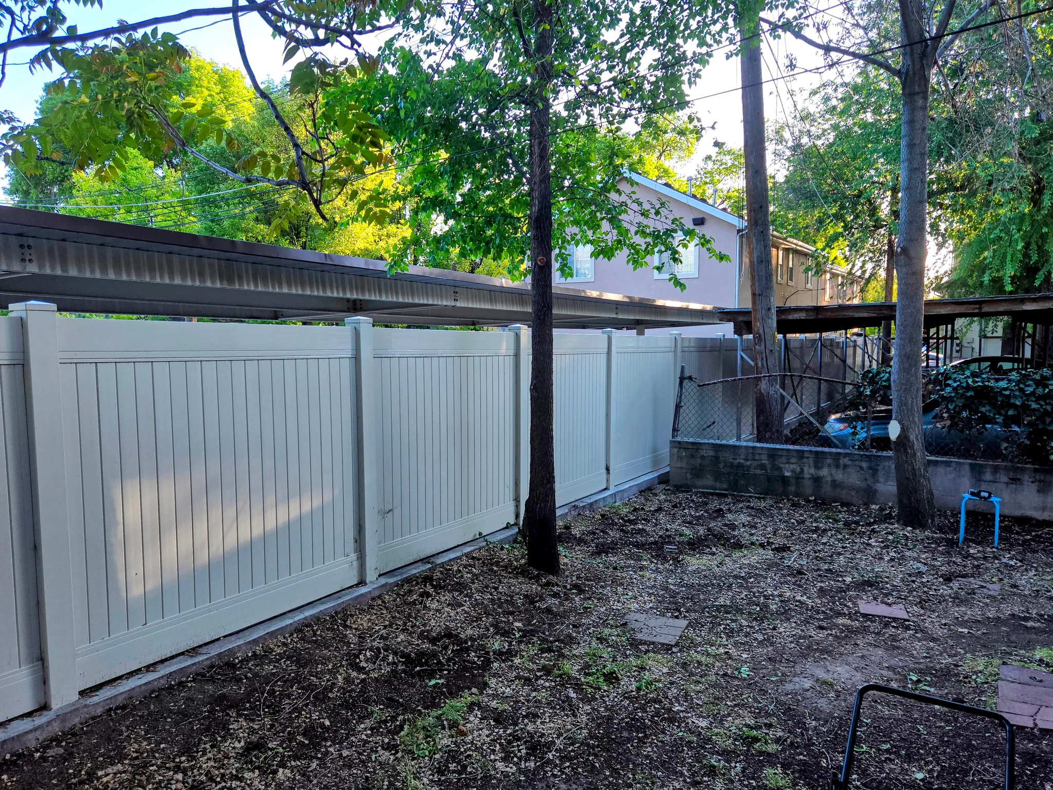 Private outdoor space featuring a light-colored solid panel fence, mature trees, and a concrete retaining wall